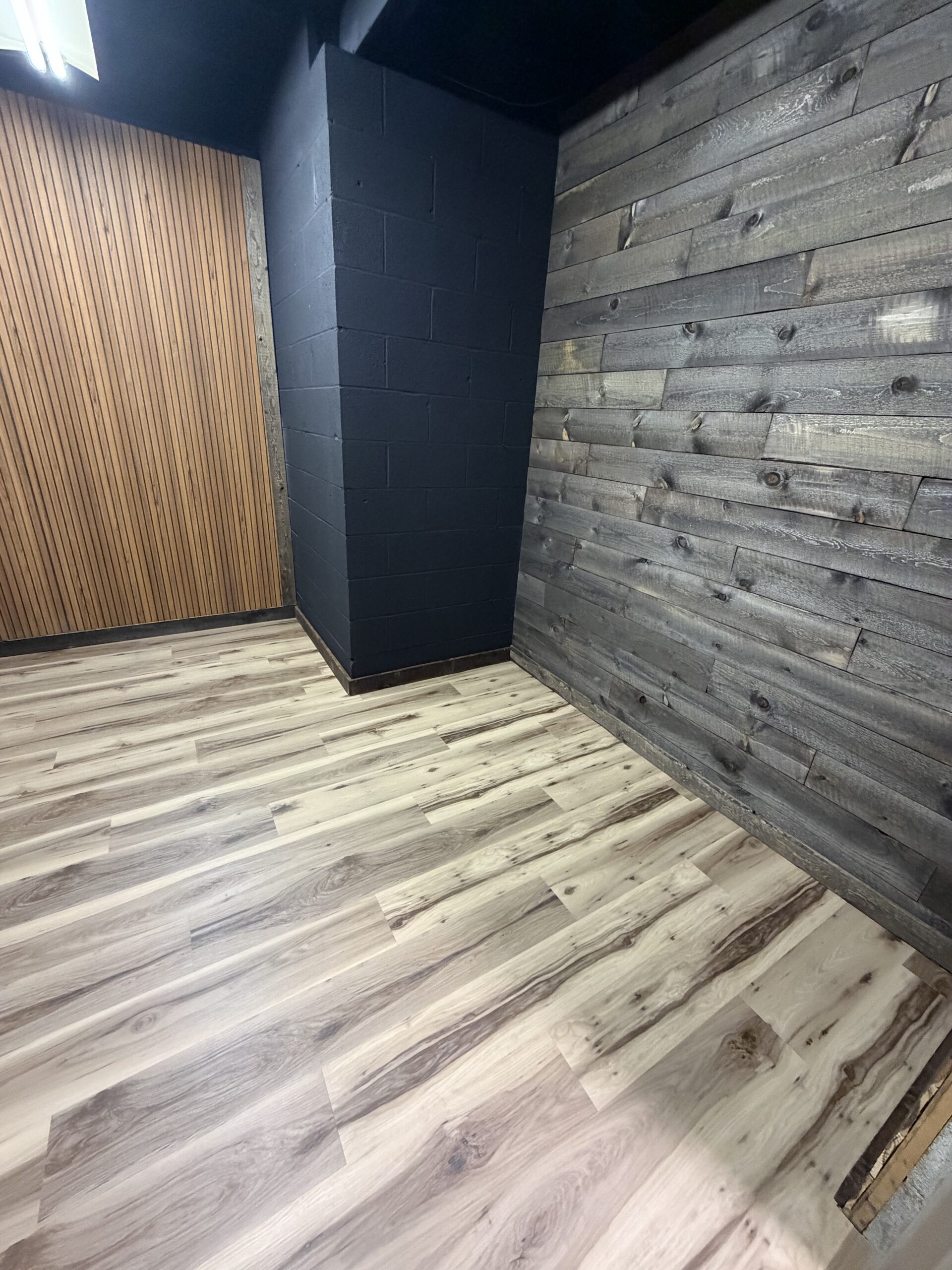 Empty room with light wood flooring, a black-painted brick wall, a vertical wooden slat wall, and a reclaimed wood accent wall.